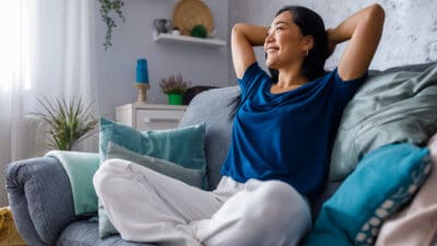 Woman smiling with her hands behind her back on her couch, symbolising passive income.