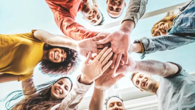 Group of young people stacking hands together in an outdoor setting. A community of multiracial international people supporting each other.