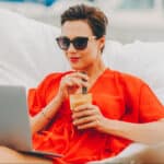 A woman in a hammock on her laptop and drinking a smoothie