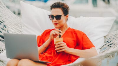 A woman in a hammock on her laptop and drinking a smoothie