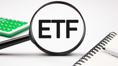 Magnifying glass on ETF text next to a calculator and notepad.