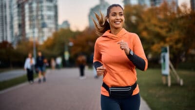 Young happy athletic woman listening to music on earphones while jogging in the park, symbolising passive income.