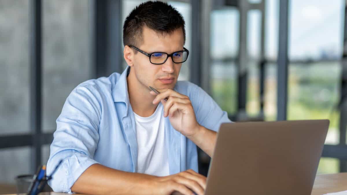 Focused man entrepreneur with glasses working, looking at laptop screen thinking about something intently while sitting in the office.