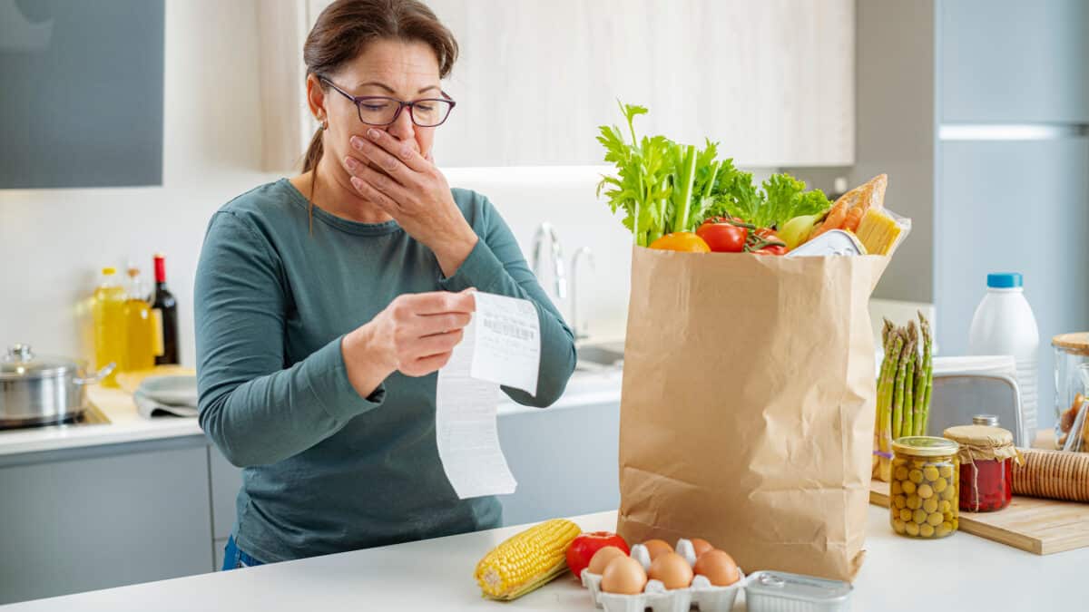 Shocked woman looking at supermarket receipt after shopping, symbolising inflation.
