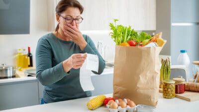 Shocked woman looking at supermarket receipt after shopping, symbolising inflation.