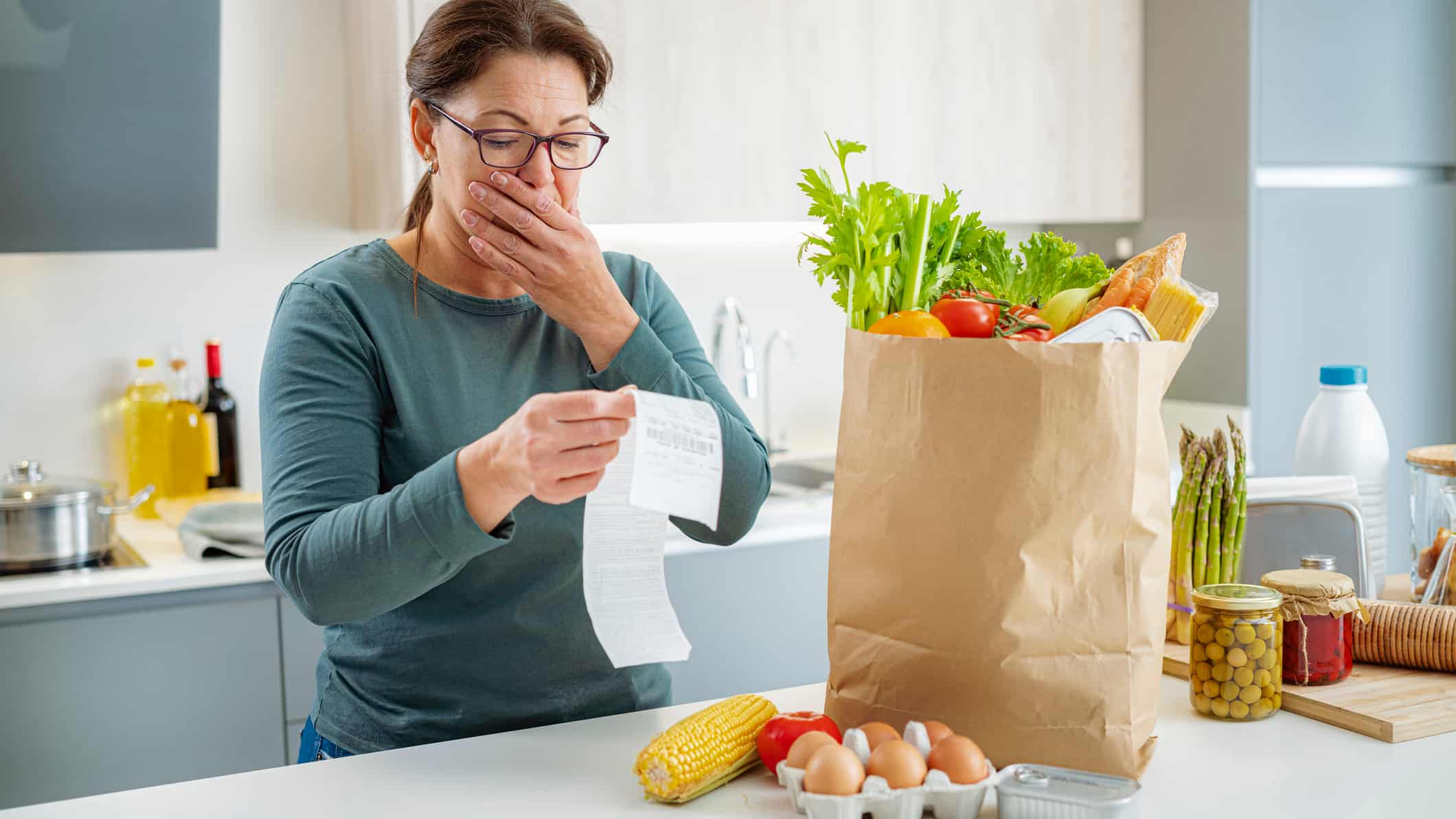 Shocked woman looking at supermarket receipt after shopping, symbolising inflation.