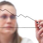 A woman draws on a clear screen a line graph that shows a falling horizontal line.