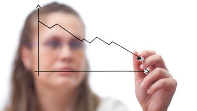 A woman draws on a clear screen a line graph that shows a falling horizontal line.