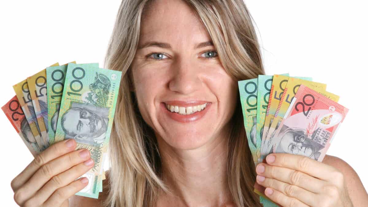 Smiling woman holding Australian dollar notes in each hand, symbolising dividends.