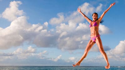 Young woman leaping into the sea with arms raised, symbolising passive income.