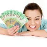 Smiling woman with her head and arm on a desk holding $100 notes out, symbolising dividends.