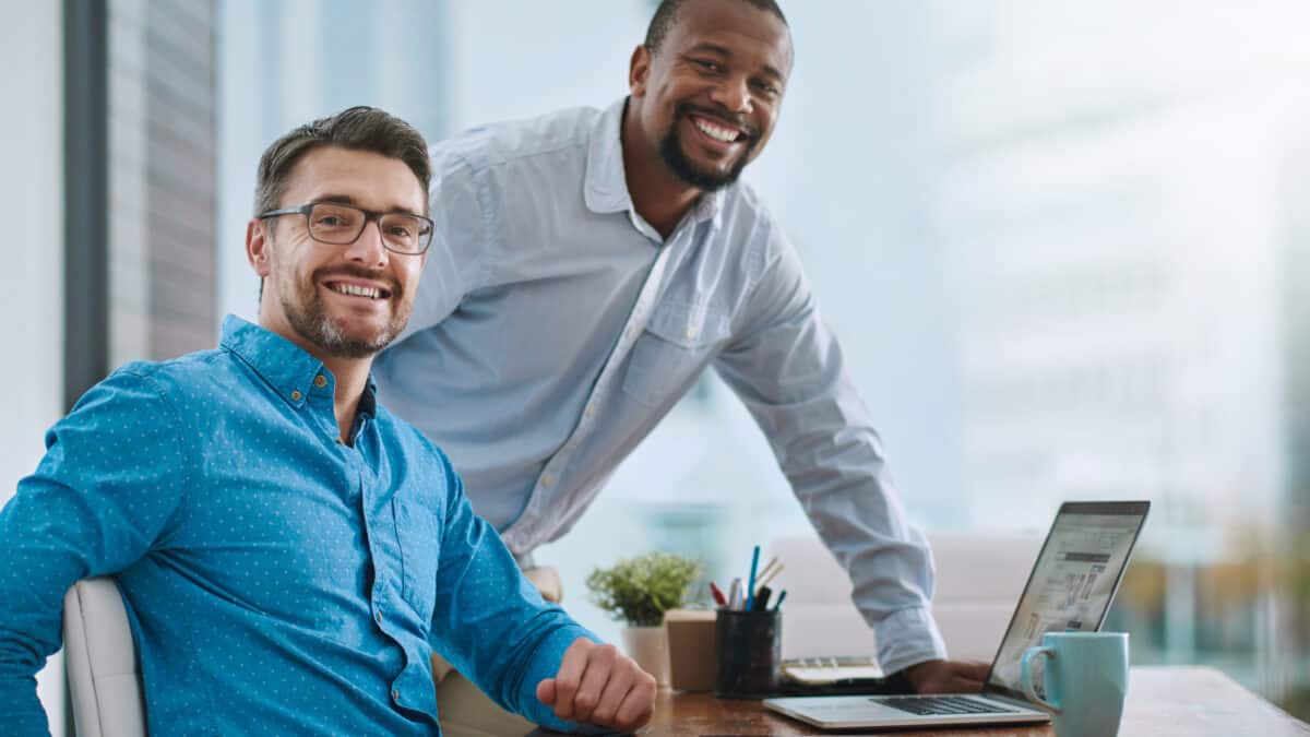 two men smiling with a laptop in front of them, symbolising a rising share price.