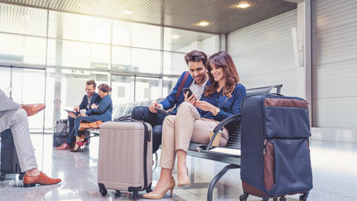 Happy couple looking at a phone and waiting for their flight at an airport.