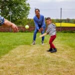 Kid swinging his bat and playing backyard cricket with his parents.