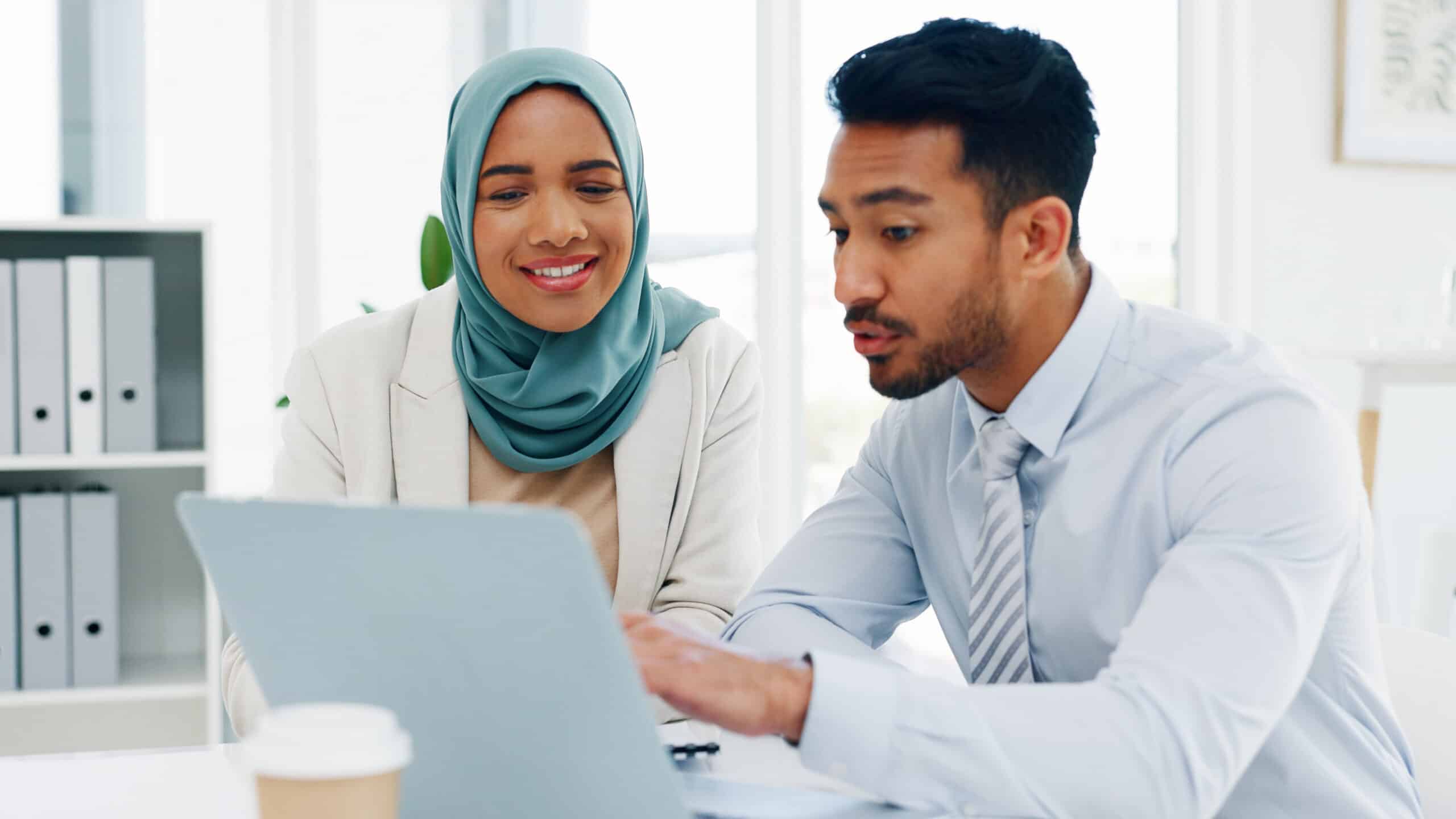 A man and woman in an office look at a laptop and discuss investing, budget strategies or other financial concepts