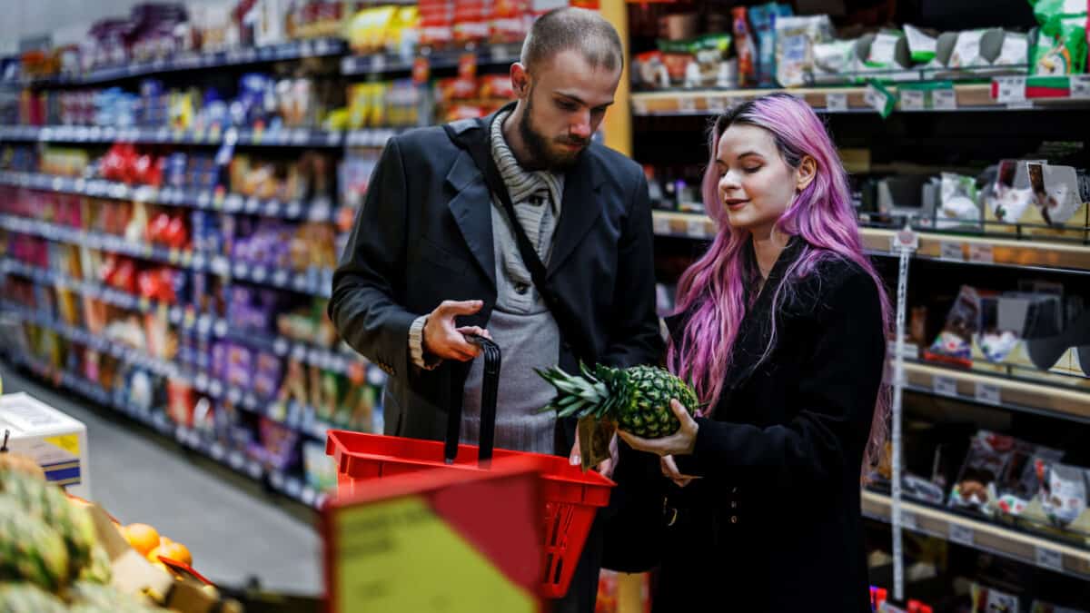 A photo of a young couple who are purchasing fruits and vegetables at a market shop.