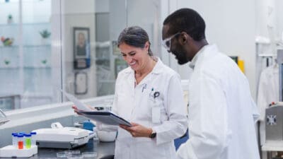 In the lab at work, the mature adult woman and young adult man smile as they review the results of their successful experimentation.