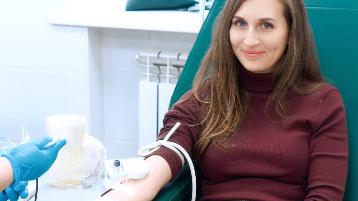Donor donates blood in medical clinic. Beautiful European woman of 30 years sits in medical chair looking into camera and smiling.