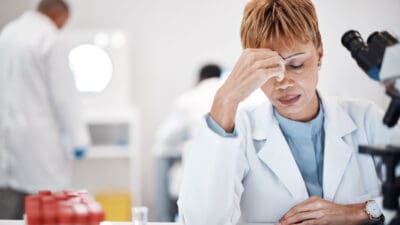 Scientist with headache, stress and fatigue with woman, overworked with overtime for science breakthrough. Medical research, scientific innovation and senior female, burnout and migraine in lab.