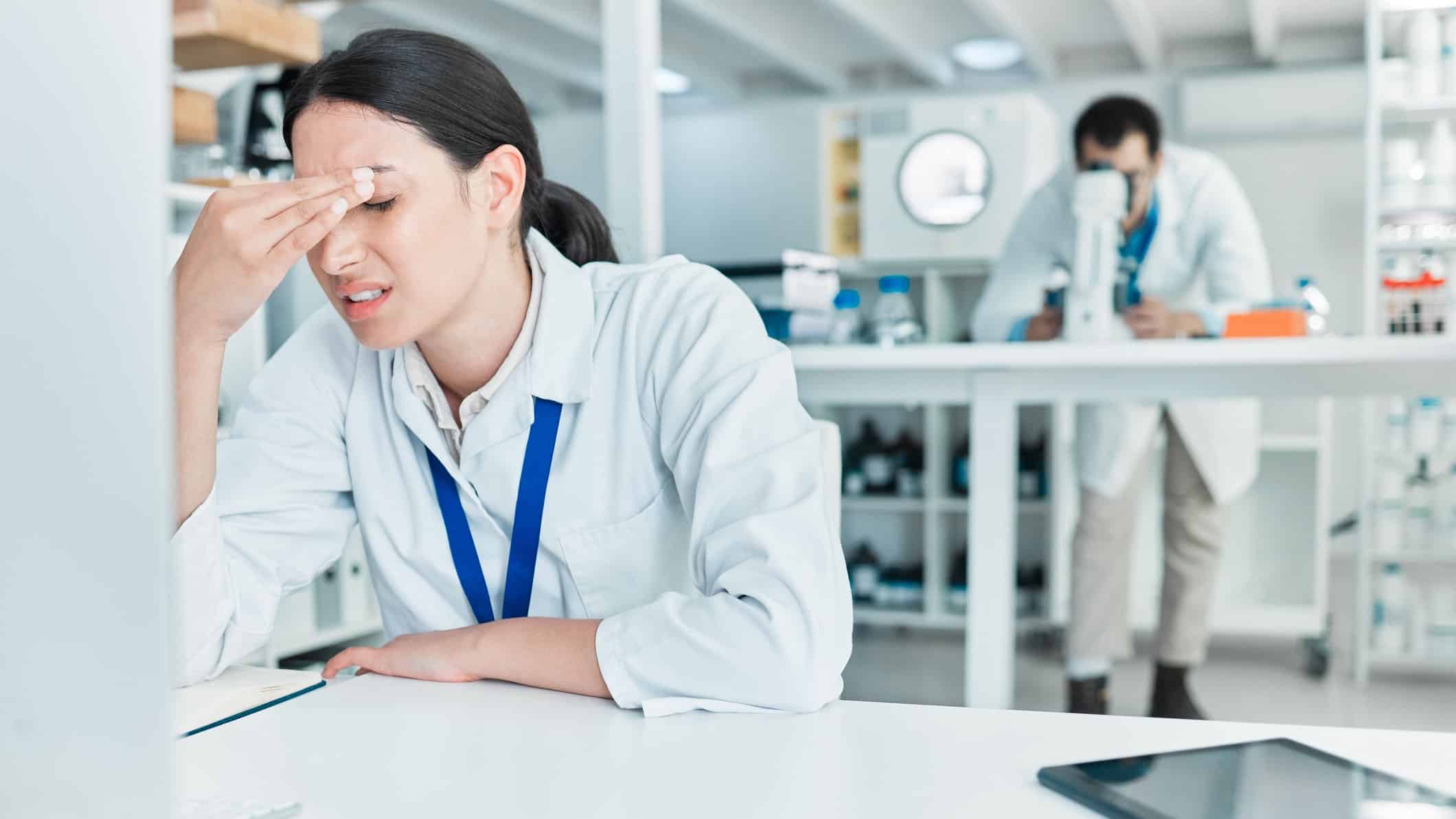Shot of a young scientist looking stressed out while working on a computer in a lab.