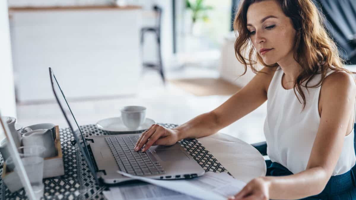 Young businesswoman sitting in kitchen and working on laptop.