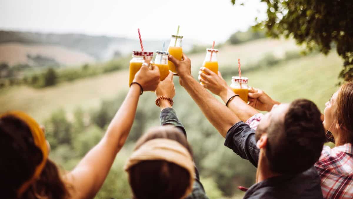 Young happy people on a farm raise bottles of orange juice in a big cheers to celebrate a dividends or financial win.