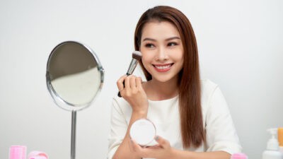 Happy woman looking in the mirror and applying cosmetic with a big brush.