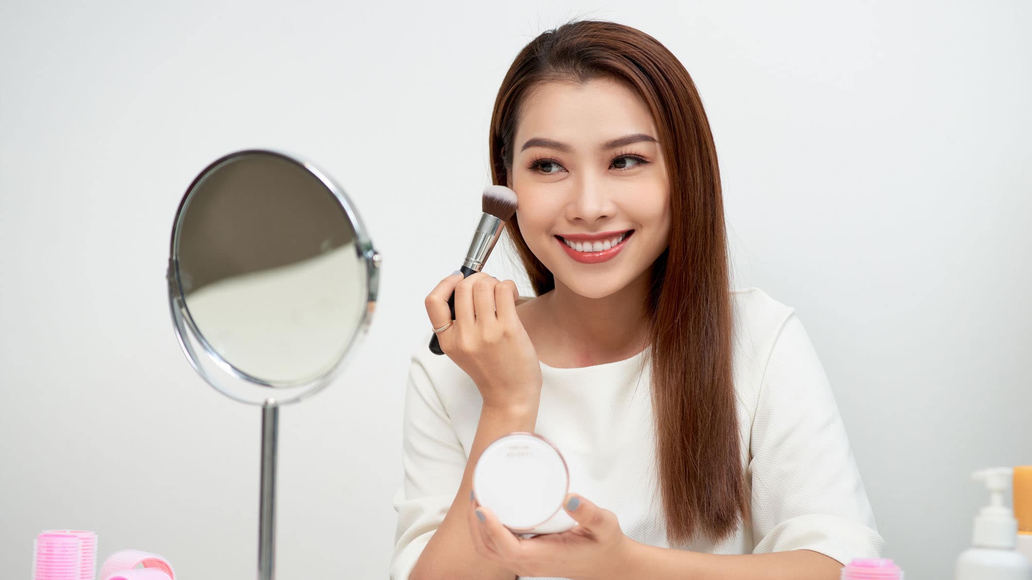 Happy woman looking in the mirror and applying cosmetic with a big brush.