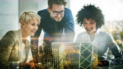 Three smiling corporate people examine a model of a new building complex.