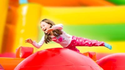 A young girl dressed in socks and pyjamas smiles as she bounces in a colourful jumping castle.