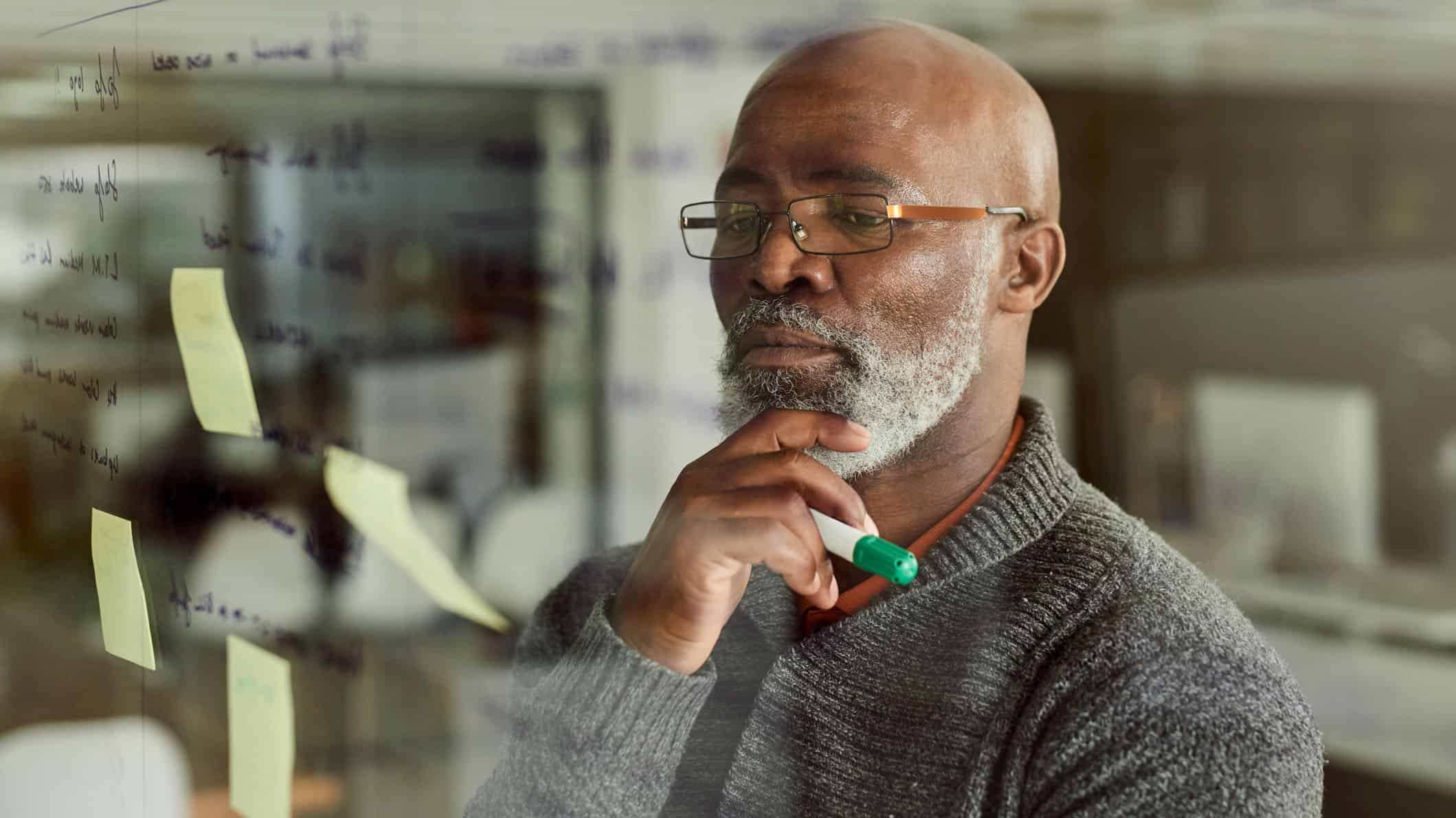 Cropped shot of a mature businessman brainstorming and setting financial goals with notes on a glass wall.