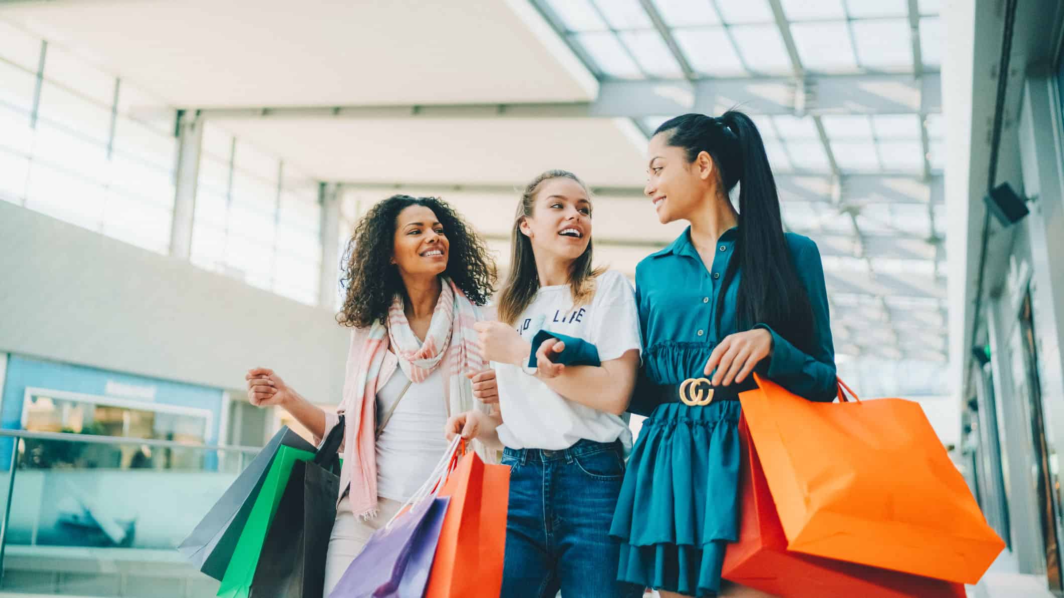 Happy friends holding shopping bags in a shopping mall.