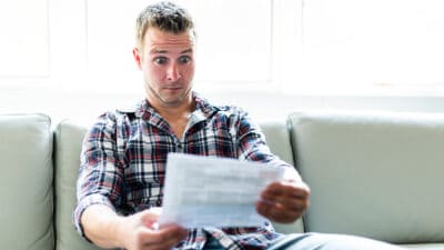 A shocked man holding some documents in the living room.
