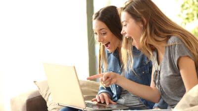Two excited woman pointing out a bargain opportunity on a laptop.