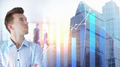 A young man looks at a stylised investment graph superimposed on an exterior office building backdrop.