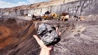 hand holding out col in front of a coal mine.