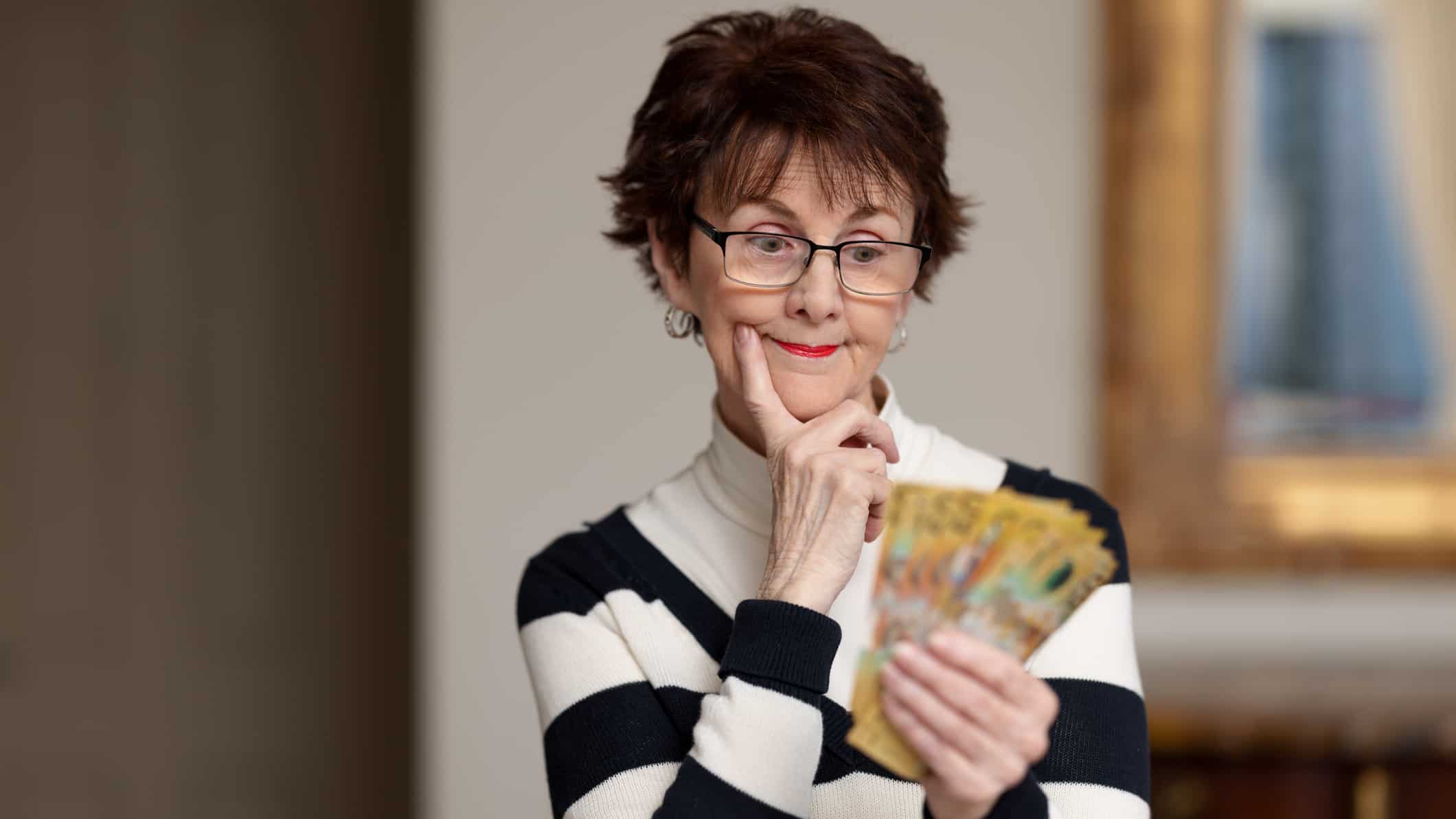 Woman with $50 notes in her hand thinking, symbolising dividends.