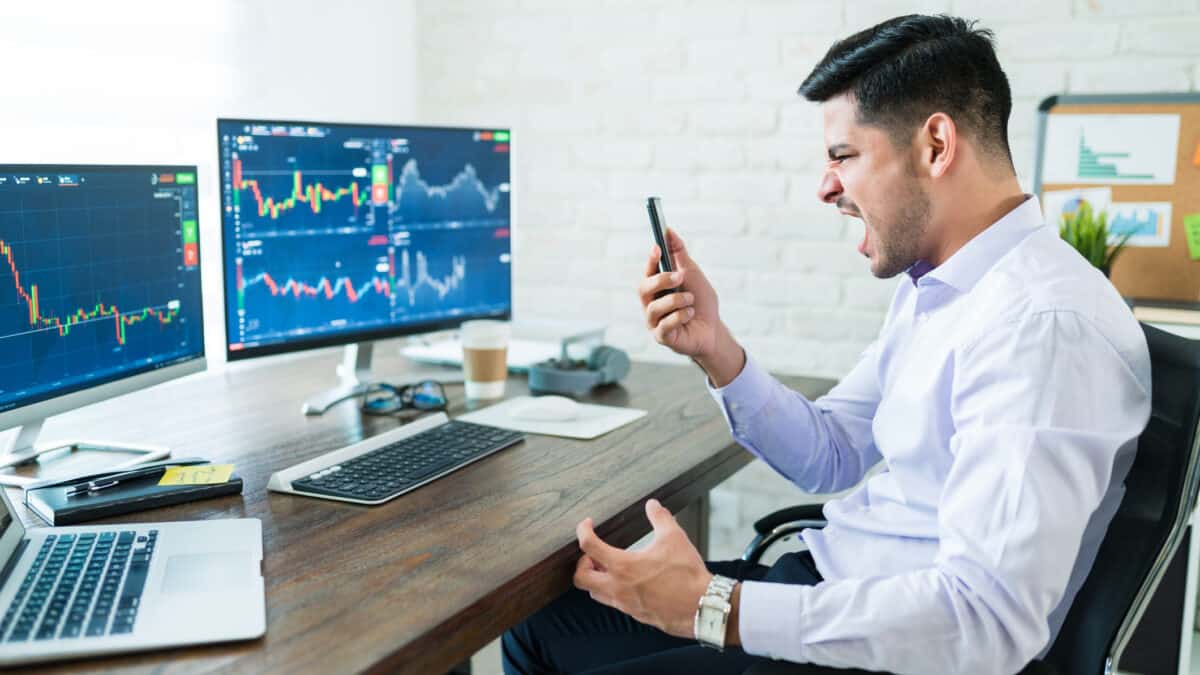 Frustrated stock trader screaming while looking at mobile phone, symbolising a falling share price.