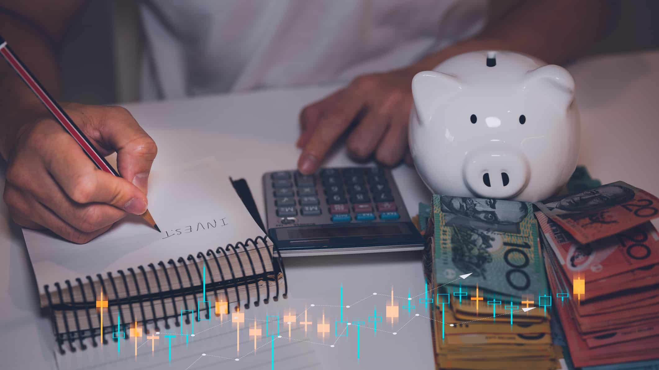 Invest written on a notepad with Australian dollar notes and piggybank.