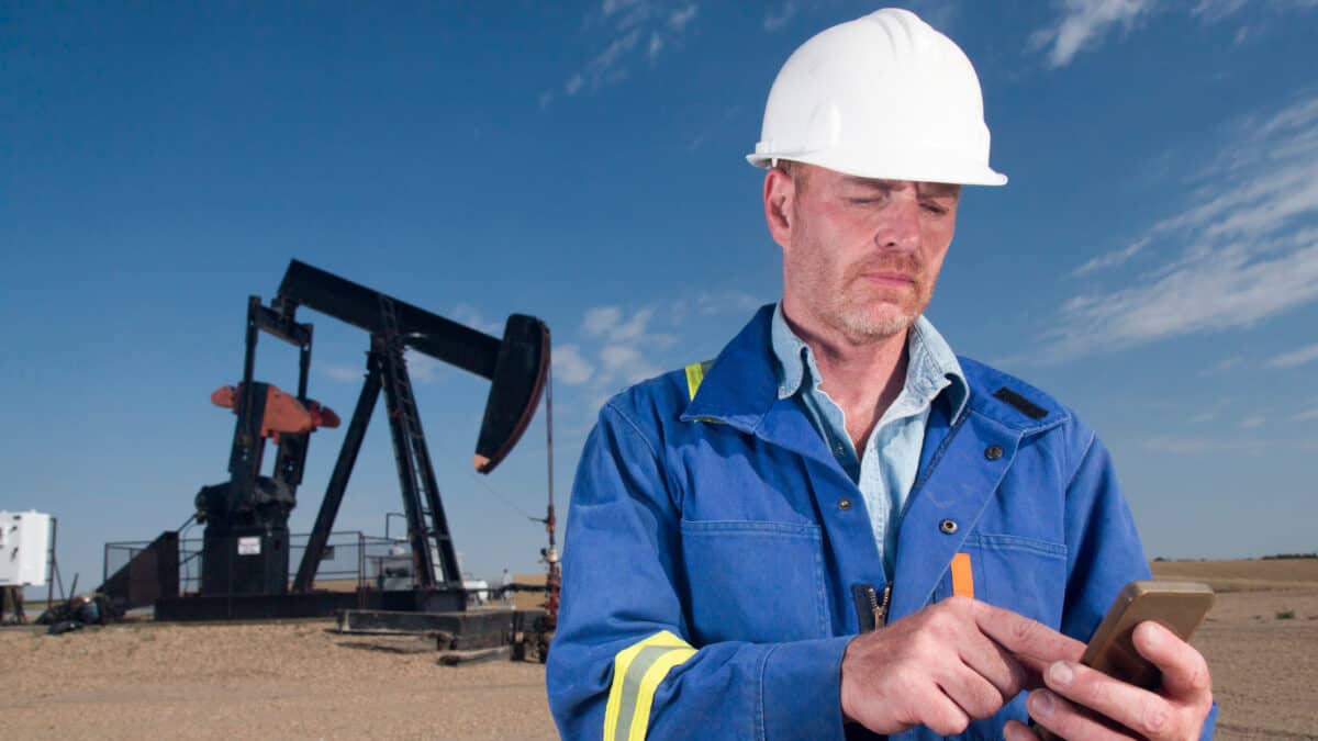 Oil worker using a smartphone in front of an oil rig.