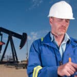 Oil worker using a smartphone in front of an oil rig.