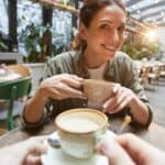 A smiling woman sips coffee at a cafe ready to learn about ASX investing concepts.
