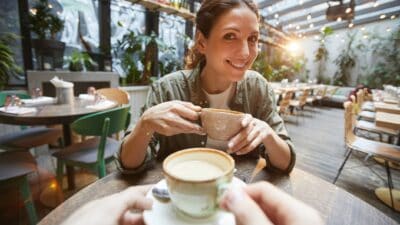 A smiling woman sips coffee at a cafe ready to learn about ASX investing concepts.