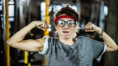 A happy woman wearing a sweatband at the gym celebrates success or an achievement by puffing up and flexing her muscles with pride.