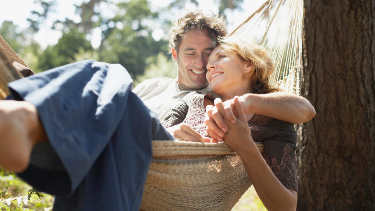A happy older couple relax in a hammock together as they think about enjoying life with a passive income stream.