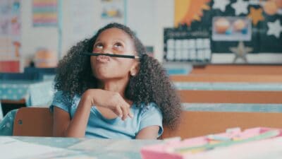A young girl looks up and balances a pencil on her nose, while thinking about a decision she has to make.