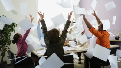 Smiling office workers fling a stack of papers into the air.