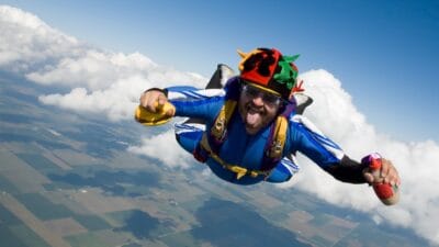 A skydiving man in a jester hat and carrying a burger and sauce, pokes out his tongue at the camera, indicating all is not lost when you're falling.