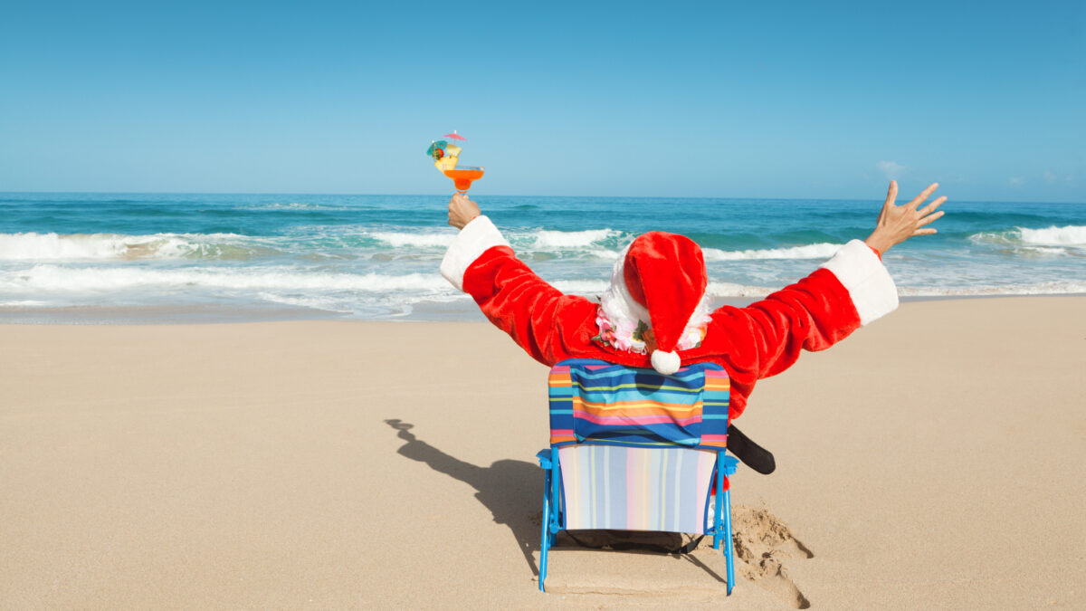 Santa Claus in a deckchair at the beach raises his arms in pleasure.