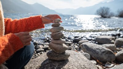 A woman stacks smooth round stones into a pile by a lake.